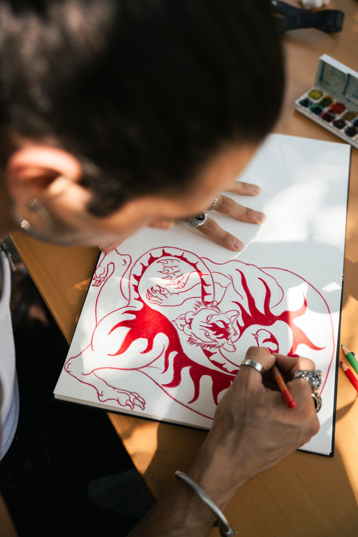 Overhead view of a finished fantasy coloring page showing a beautifully colored dragon with rich jewel tones and metallic effects, colored pencils arranged by color family nearby, satisfying completed artwork, warm dramatic lighting