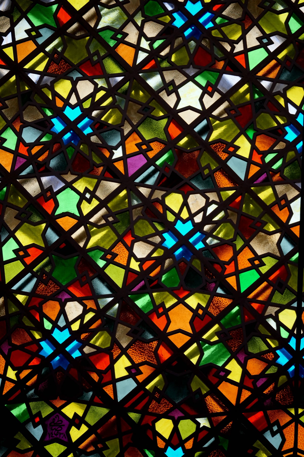 Close-up of hands coloring a stained glass design with jewel-toned colored pencils, bold black lines visible between sections, focused and precise technique, warm desk lighting, artistic process