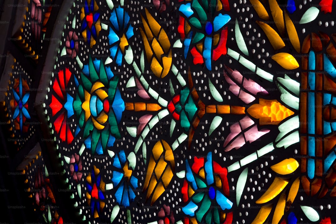 Finished stained glass coloring page held up against a bright window, light glowing through the jewel-toned colored sections creating a beautiful stained glass effect, bold black lines framing each color panel, satisfying and beautiful result