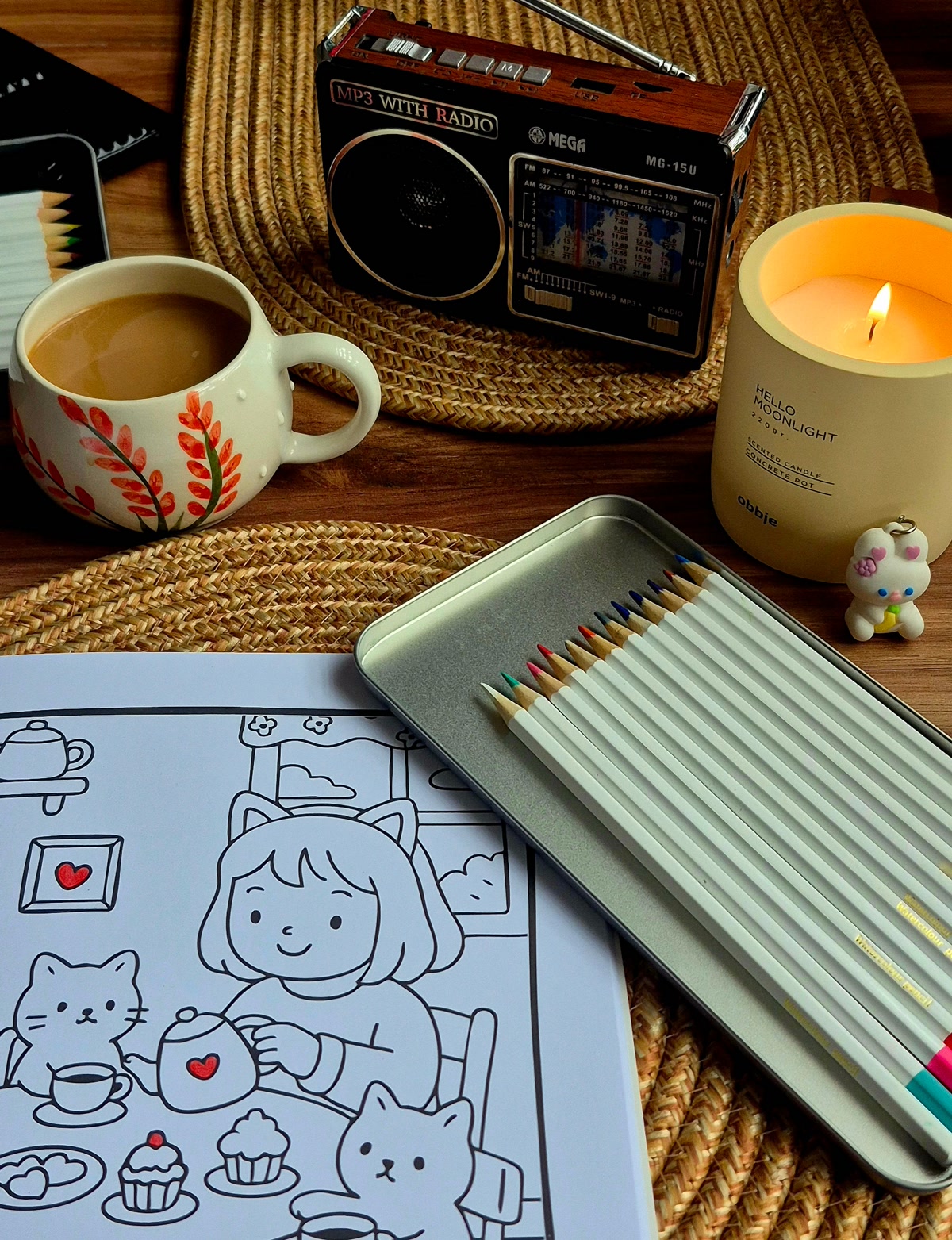A calm coloring setup with an open mindfulness coloring book, a few colored pencils, a lit candle, and a cup of tea on a wooden table, soft evening light, peaceful atmosphere, overhead shot