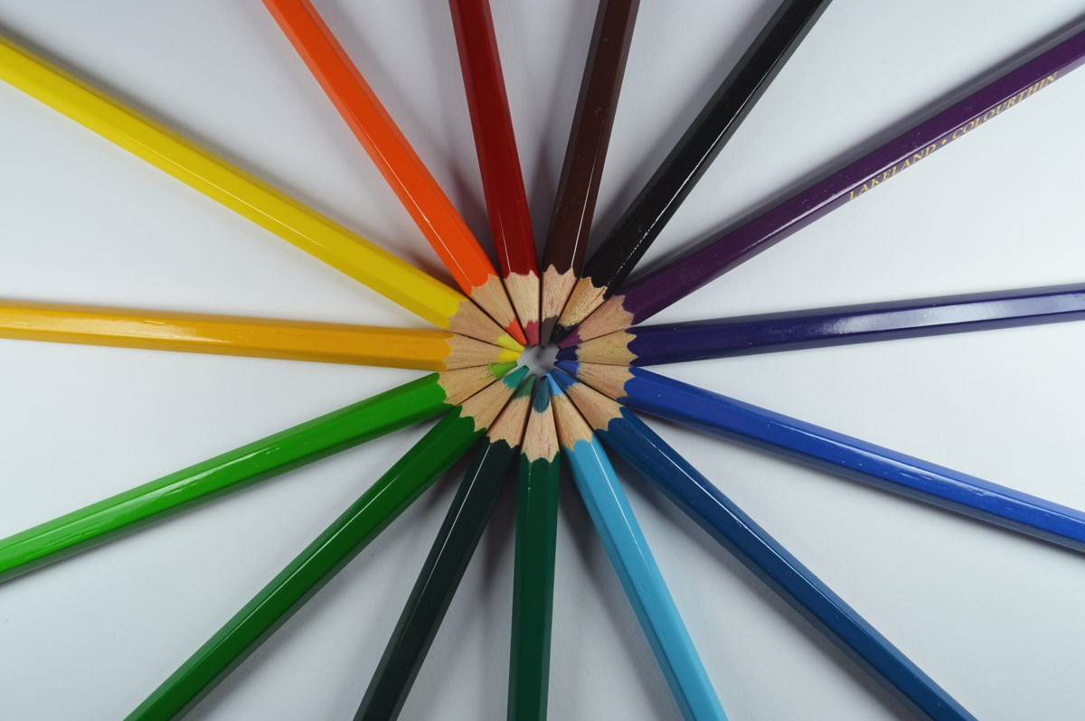 A color wheel alongside an open adult coloring book with colored pencils arranged by hue, warm and cool tones visible, lifestyle photography