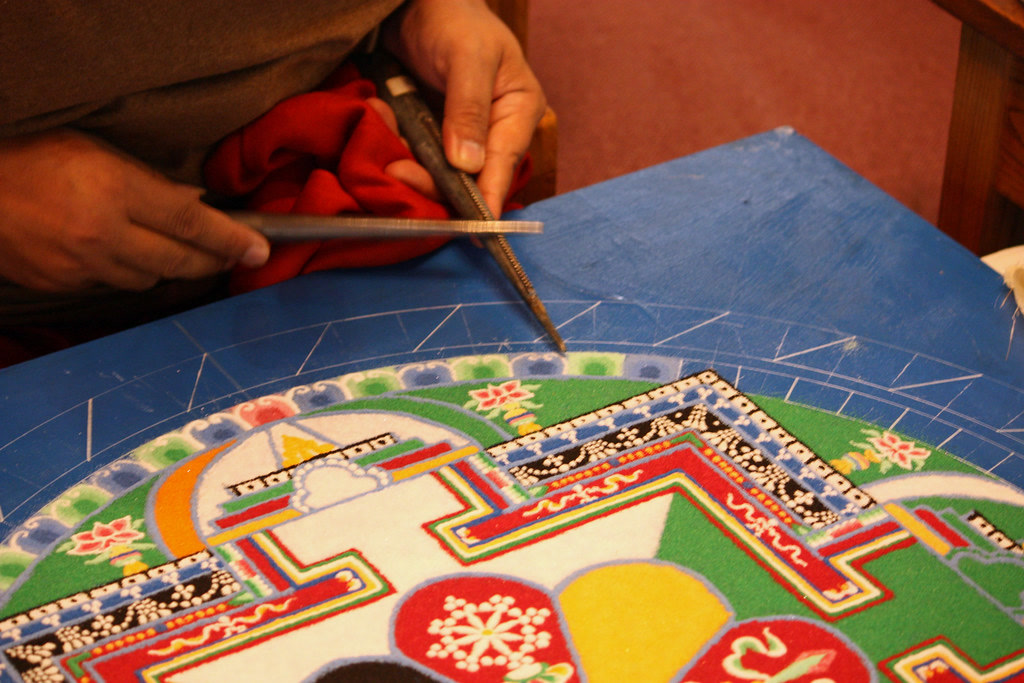 Hands coloring a mandala page using analogous warm colors from yellow through orange to red, smooth gradient transitions, colored pencils visible