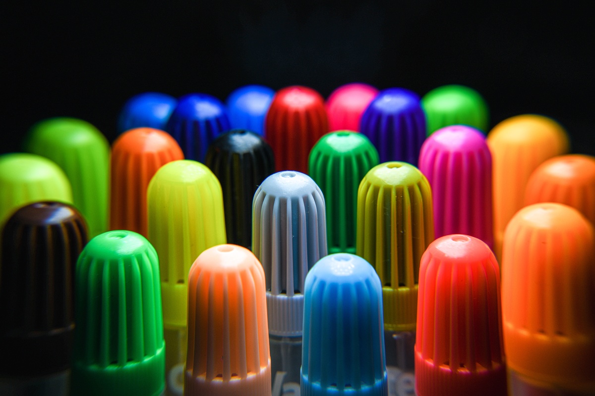 An array of Crayola adult coloring markers in various tip styles laid out on a white surface, dual-tip markers showing both ends, vibrant color range visible, product photography