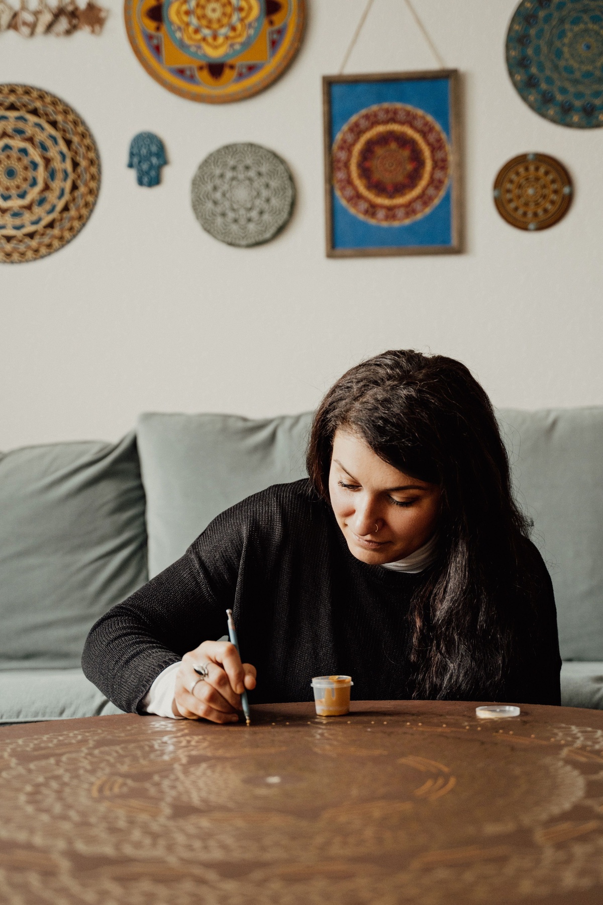 Hands coloring a mandala with focused precision, colored pencils fanned out beside the book, a phone timer visible showing 15 minutes, warm desk lighting, close-up lifestyle photography