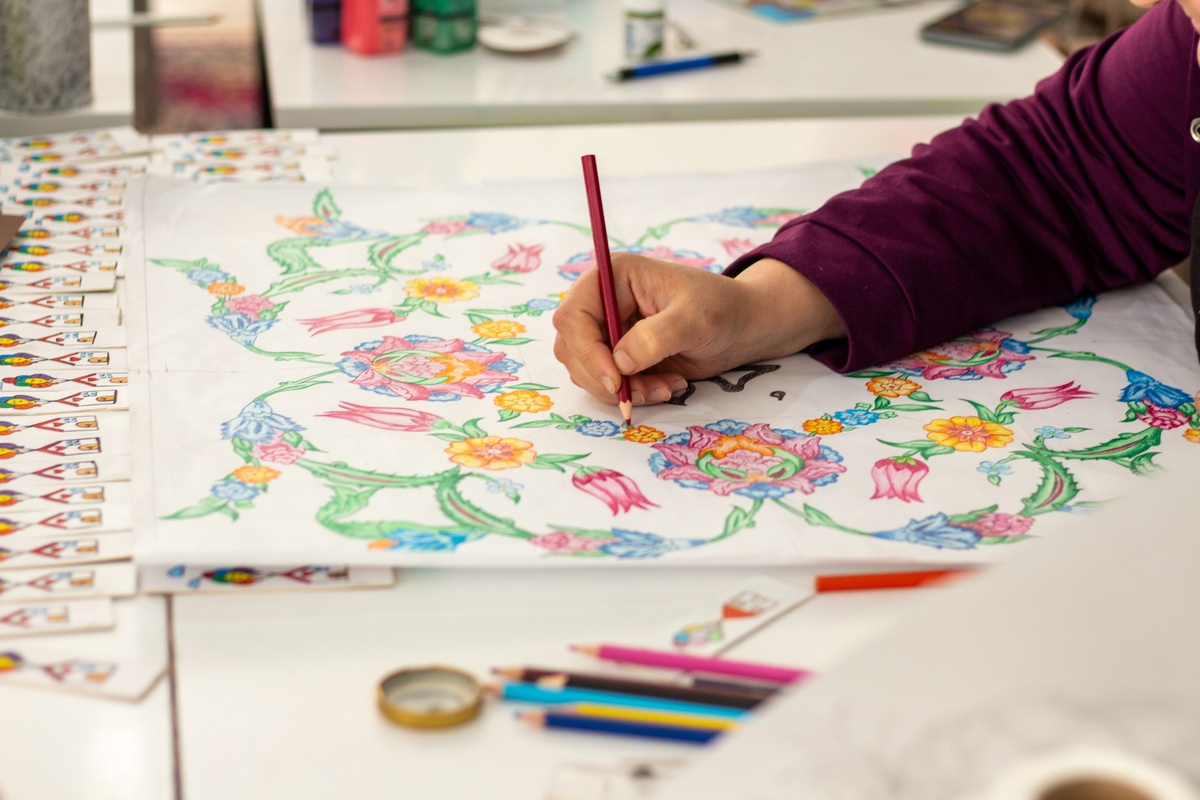 A partially completed coloring page showing distinct sections filled in one at a time, colored pencils arranged by color family, satisfying progress visible, warm lighting, flat lay photography