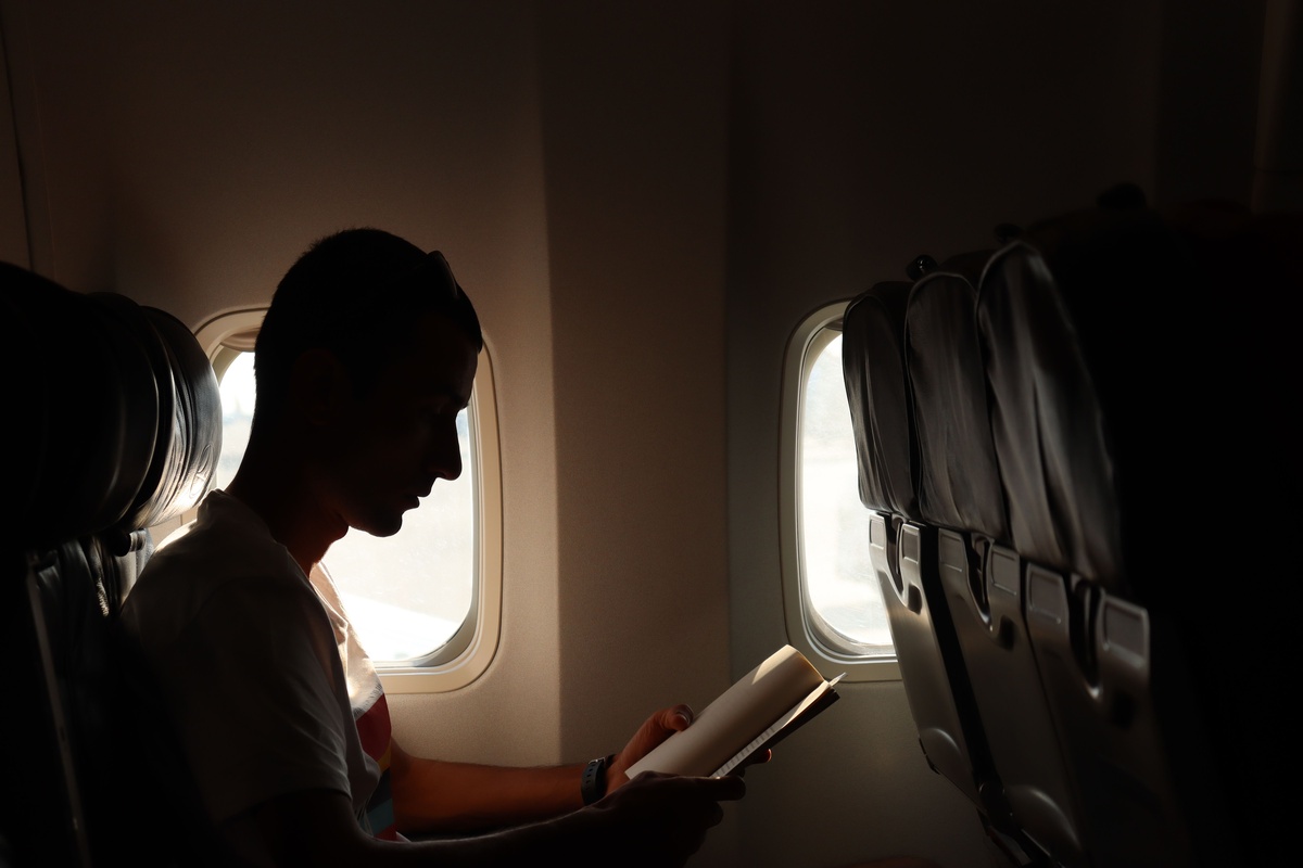Person reading by an airplane window, natural light streaming in from the window