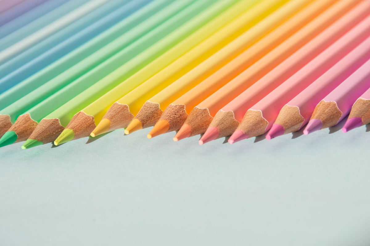 A printed color wheel chart next to an assortment of colored pencils sorted by color family, warm tones on one side and cool tones on the other, overhead photography