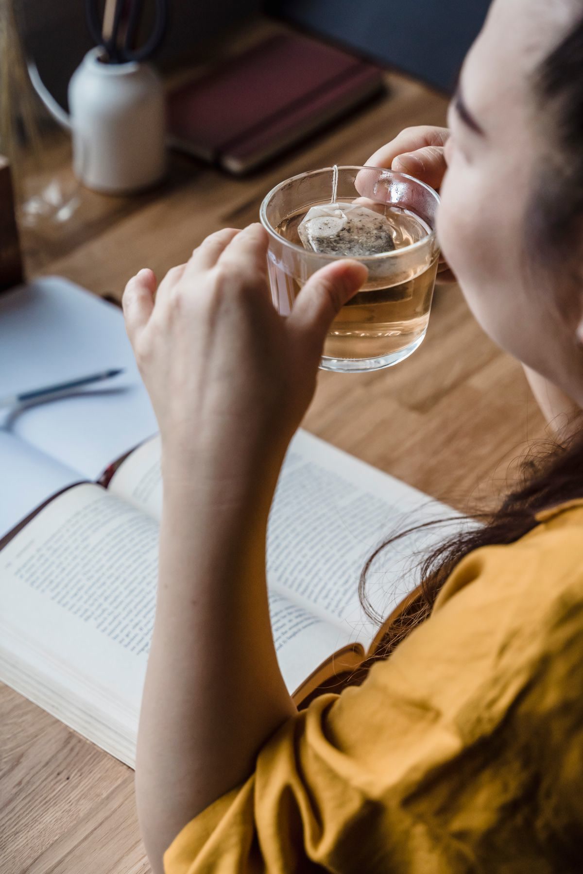 A woman sitting comfortably at a small table coloring in a mindfulness coloring book, soft warm lighting, a cup of tea beside her, colored pencils arranged neatly, peaceful and cozy atmosphere, lifestyle photography
