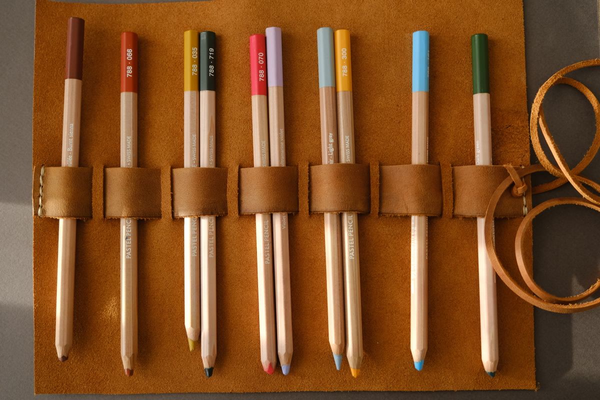 Kum brass pocket sharpener next to colored pencils in a travel coloring kit
