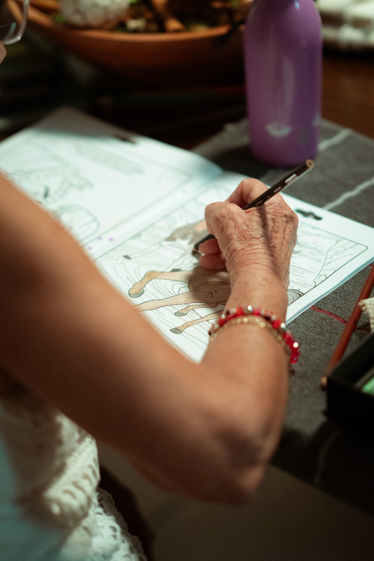 Close-up of elderly hands holding a thick triangular colored pencil, coloring a simple bold design on large-print paper, warm lighting, gentle and careful movements, peaceful scene
