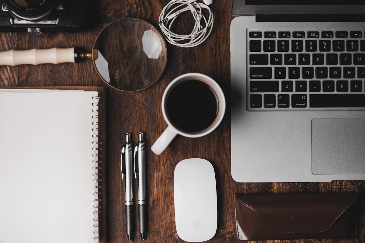 Top-down view of a workspace with notebook, pens, and coffee on a wooden desk