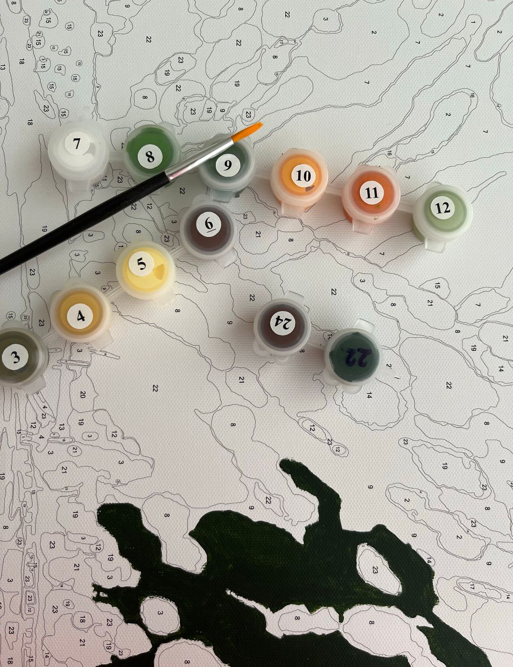 A paint by numbers set with numbered paints and brush on a canvas, adult coloring activity